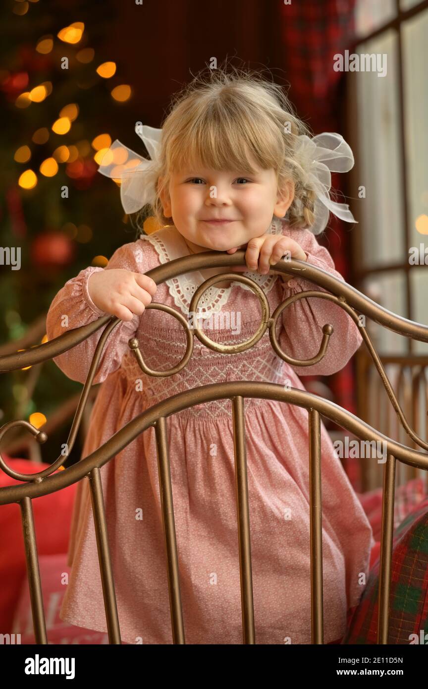 Bambina carina bionda in piedi alla testata del letto di ferro Foto Stock