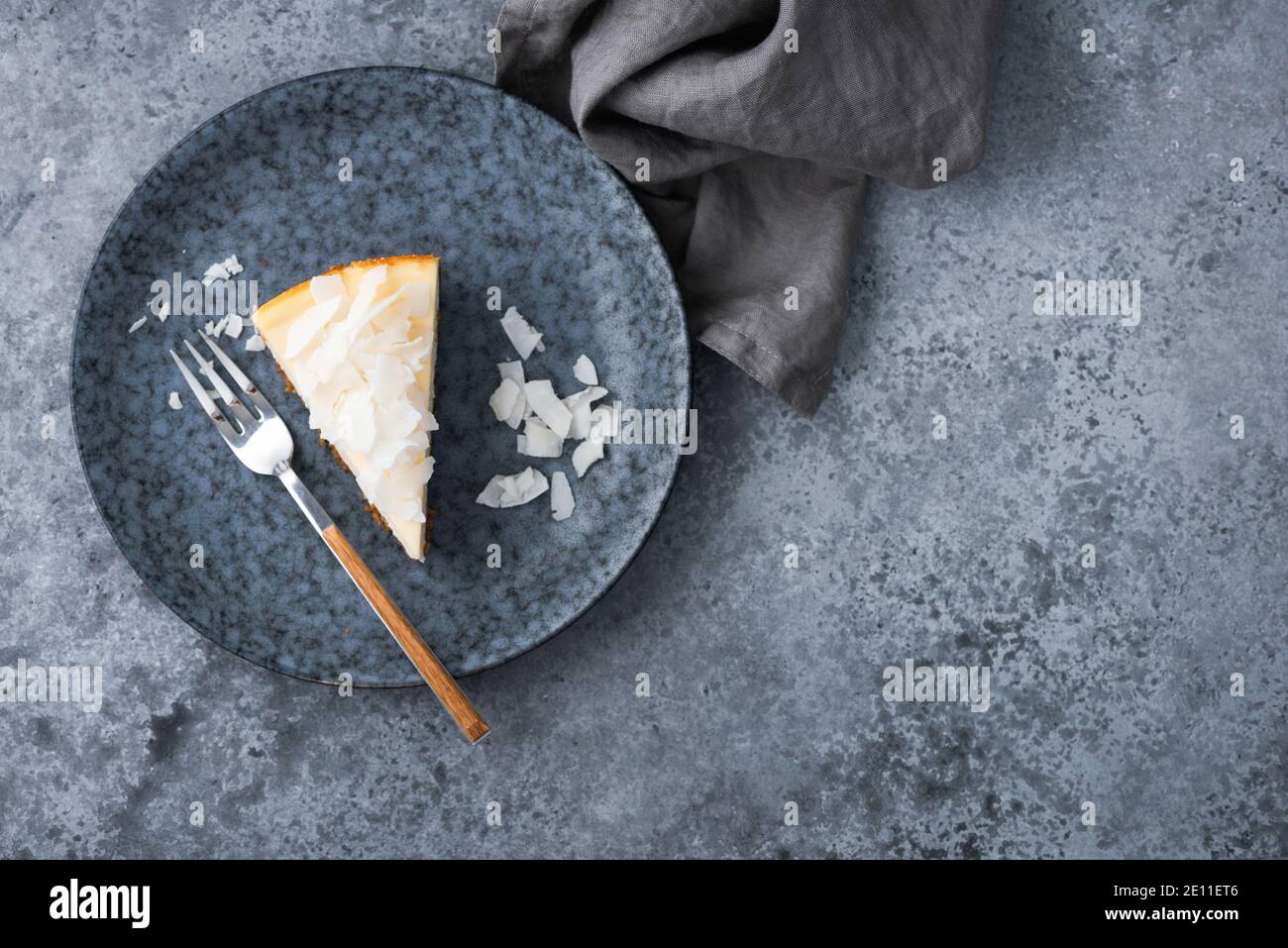 Fetta di torta di cocco vegana su un piatto blu, vista dall'alto. Cheesecake proteico a base vegetale vegana Foto Stock