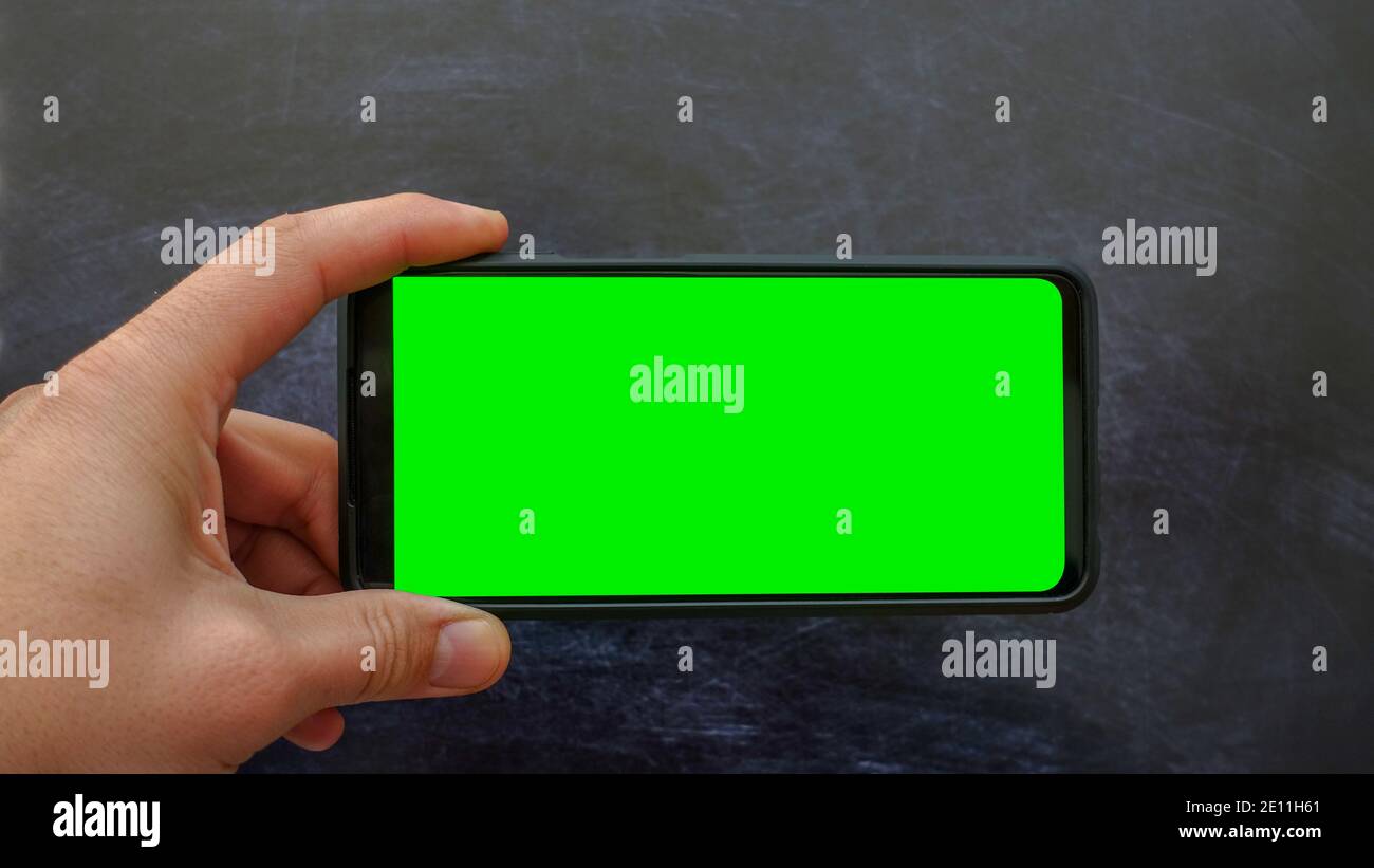 Telefono cellulare con schermo verde verticale con spazio per testo e design. Pubblicità app mobile. Giovane maschio con uno smartphone moderno. Chiave Chroma Foto Stock