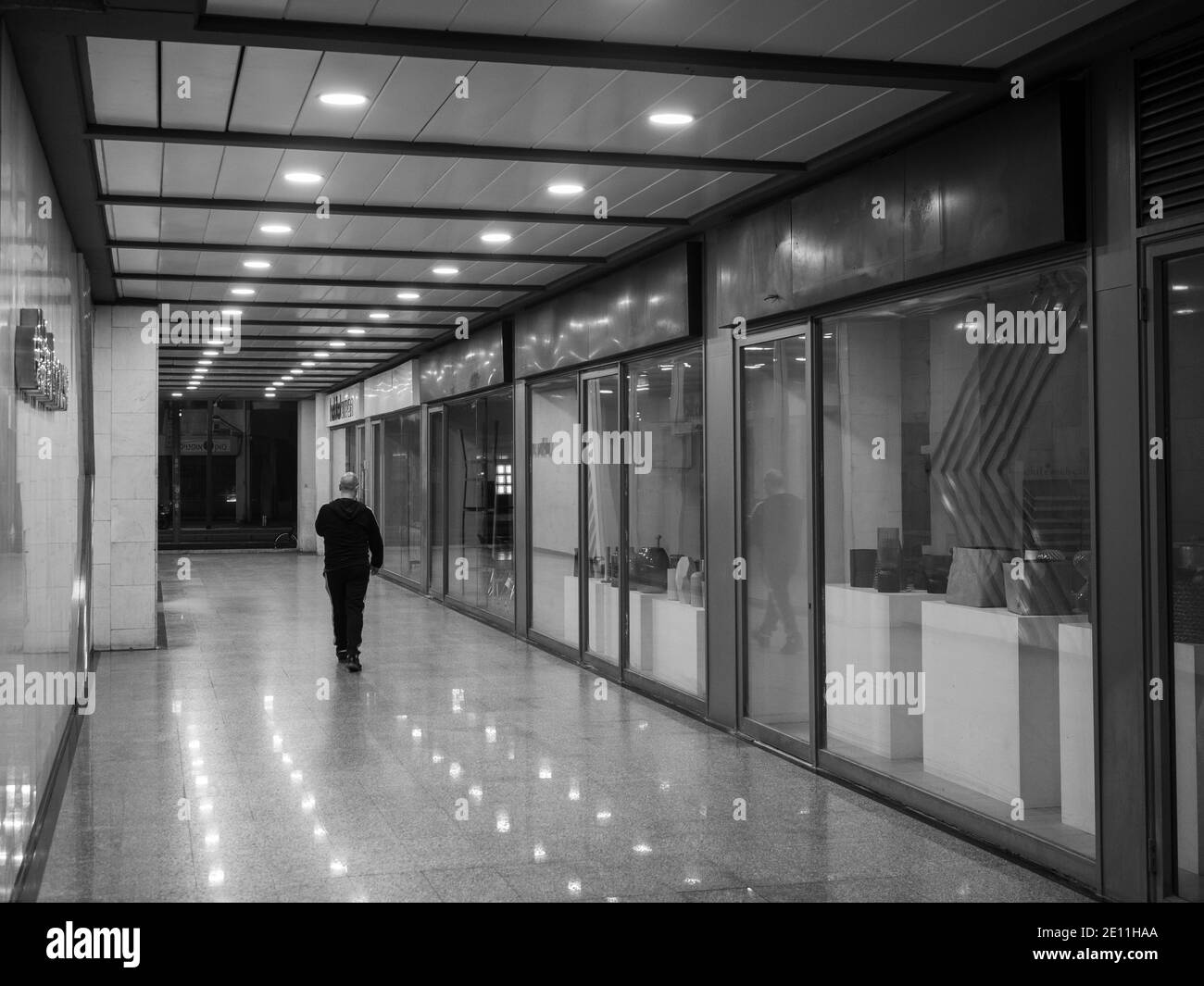 Un uomo che cammina di notte attraverso il passaggio di strada con negozi. Foto Stock