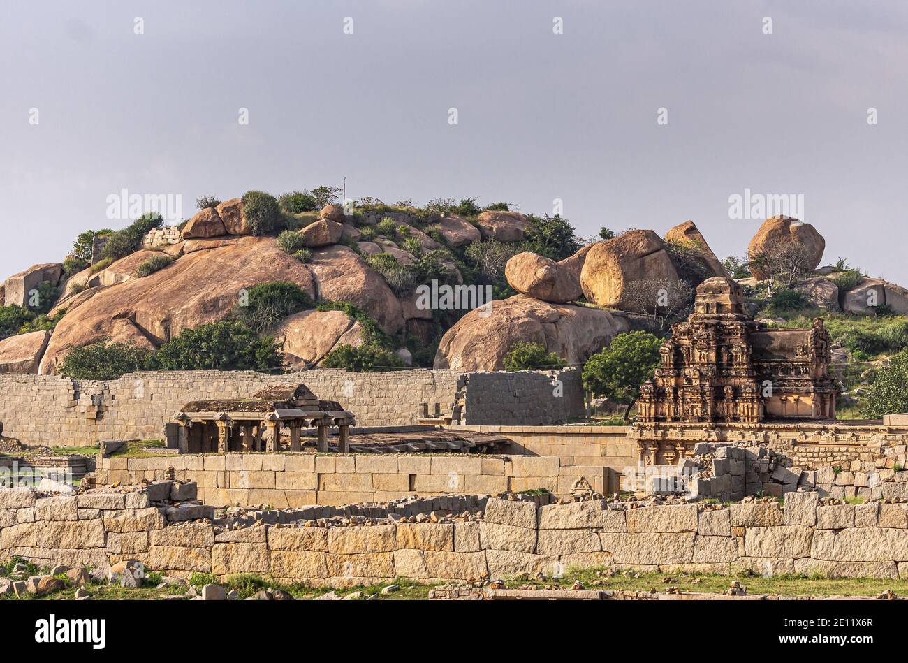 Hampi, Karnataka, India - 4 novembre 2013: Il tempio di Hazare Rama si nasconde dietro le rovinose pareti beige del recinto reale. Cielo azzurro e grande marrone bo Foto Stock