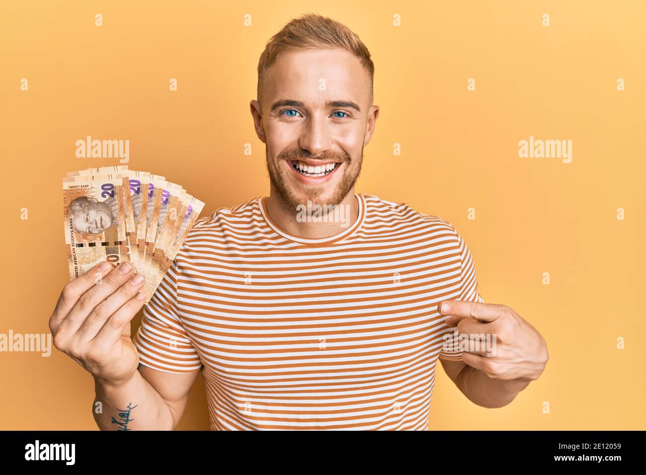 Giovane caucasico che tiene in mano banconote da 20 rand sudafricane sorridenti buon puntamento con mano e dito Foto Stock