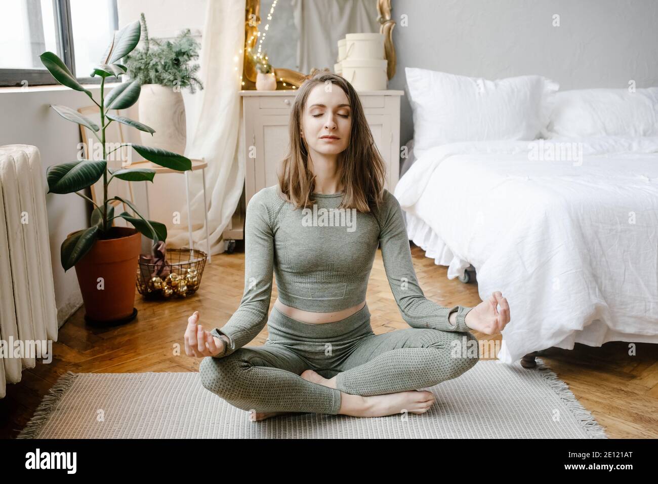 Giovane donna fitness che pratica yoga sul pavimento in camera da letto a casa al mattino. Sport ragazza facendo meditazione in lotus posa esercizio in interni. Salute dell'allenamento Foto Stock