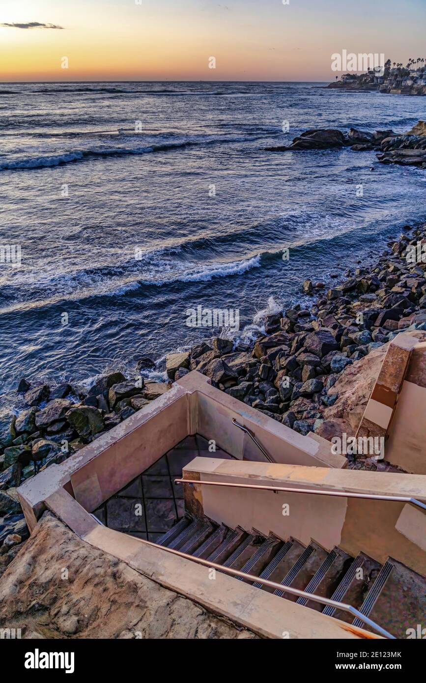 Scale che conducono giù alla costa rocciosa dell'oceano con il tramonto e cielo all'orizzonte Foto Stock