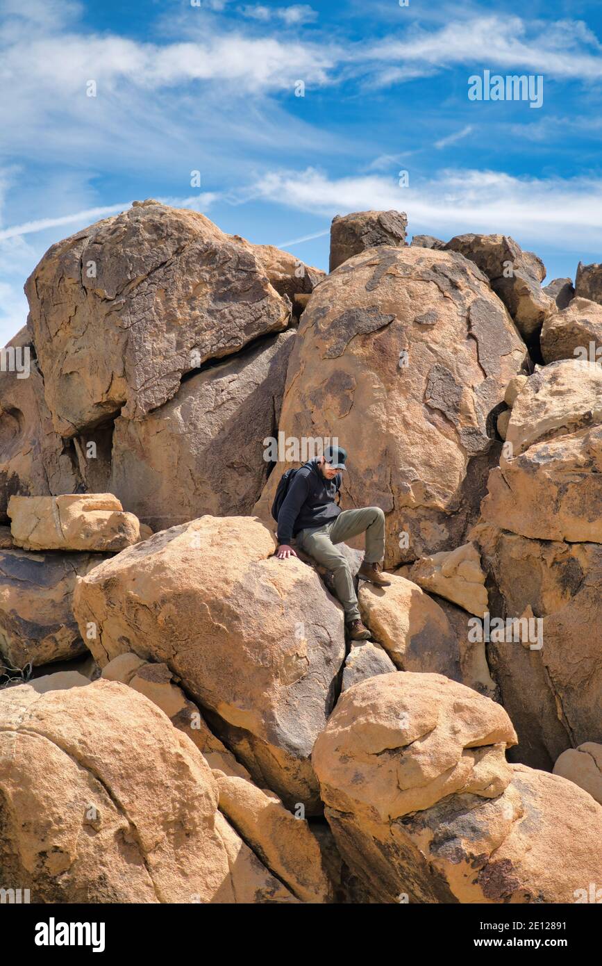 Uomo seduto su enormi rocce contro cielo blu nuvoloso a. Parco Nazionale di Joshua Tree Foto Stock