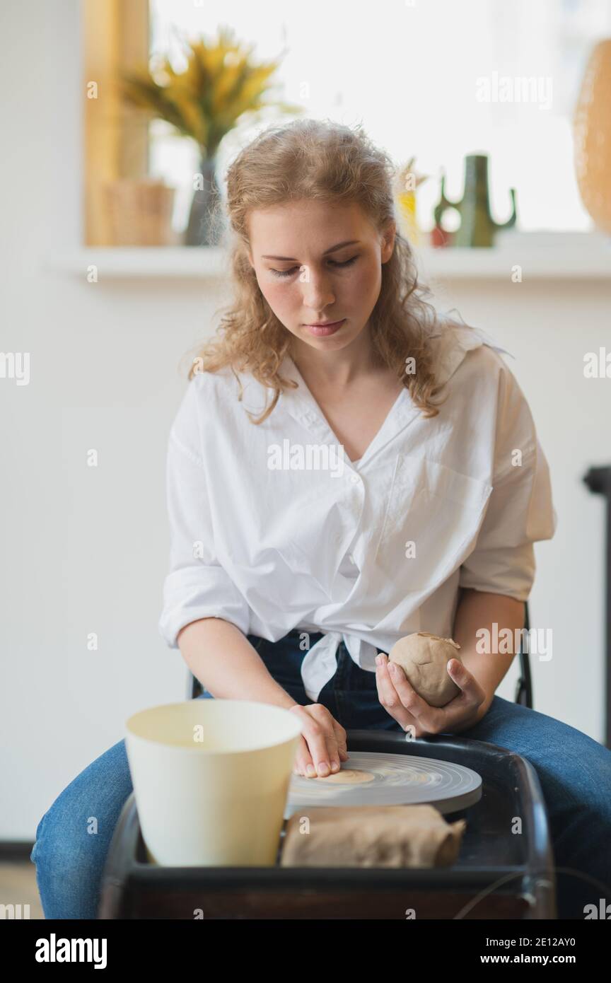 Vista ravvicinata delle mani della donna che lavorano sulla ruota in ceramica e che fanno pentola di argilla. Le mani scolpisce una tazza da pentola di argilla. Workshop sulla modellazione del vasaio Foto Stock