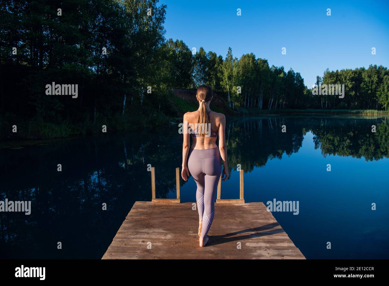 La ragazza sta praticando la tecnica di yoga sul molo vicino al lago e meditando. Meditazione per purificare la mente e la calma. Foto Stock