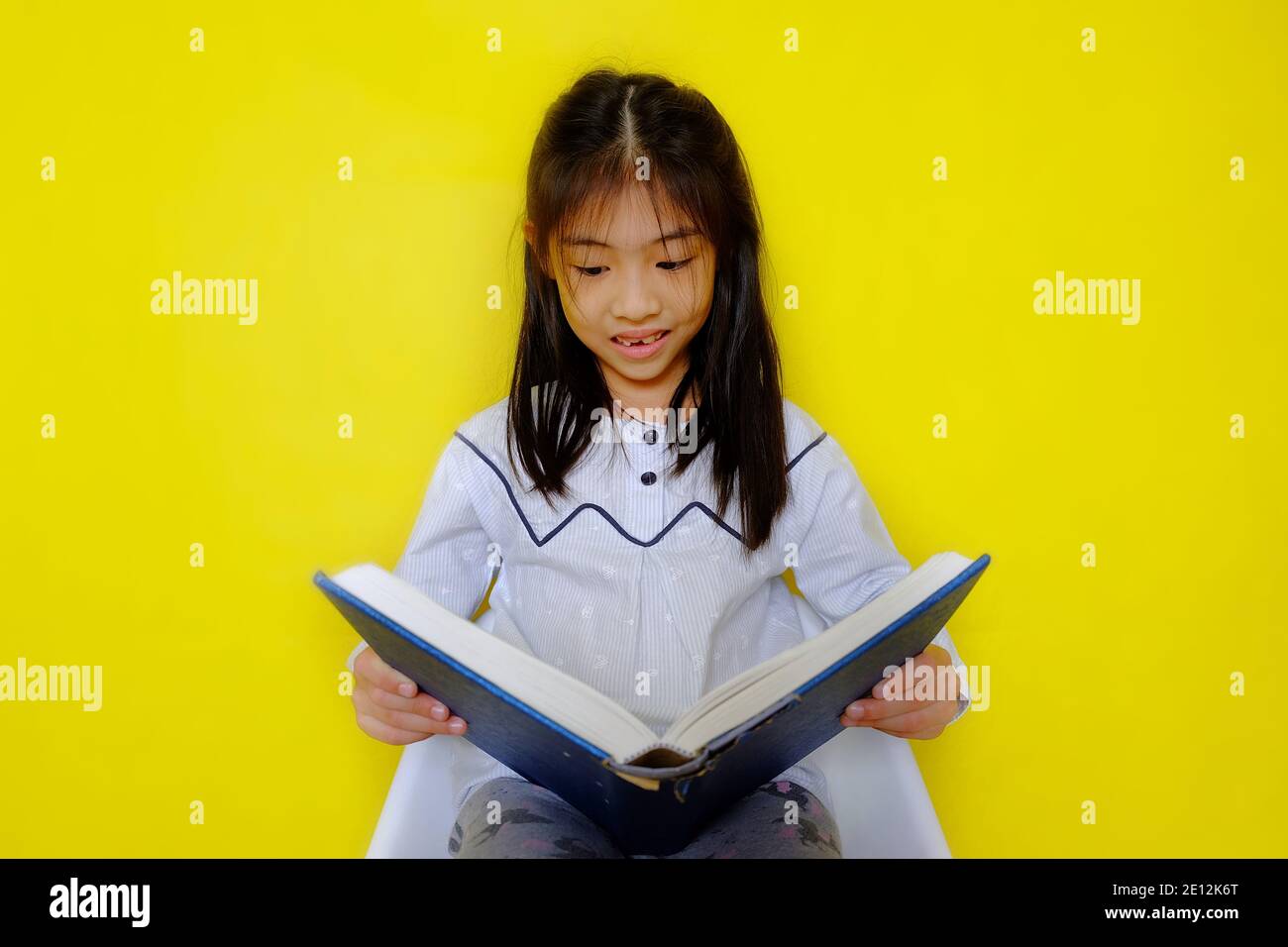 Una giovane ragazza asiatica carina che tiene un libro di storia, la lettura e godendo. Sfondo giallo brillante. Foto Stock