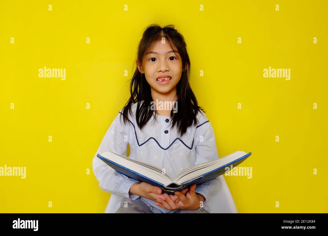 Una giovane ragazza asiatica carina che tiene un libro di storia, la lettura e godendo. Sfondo giallo brillante. Foto Stock