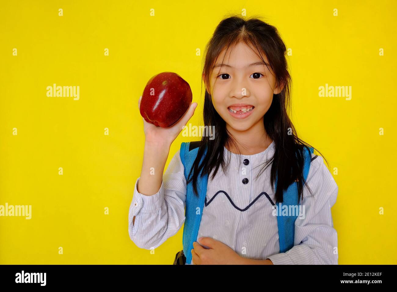 Una giovane ragazza asiatica carina che tiene in mano una mela, preparandosi a mangiarla per la prima colazione. Sfondo giallo brillante. Foto Stock