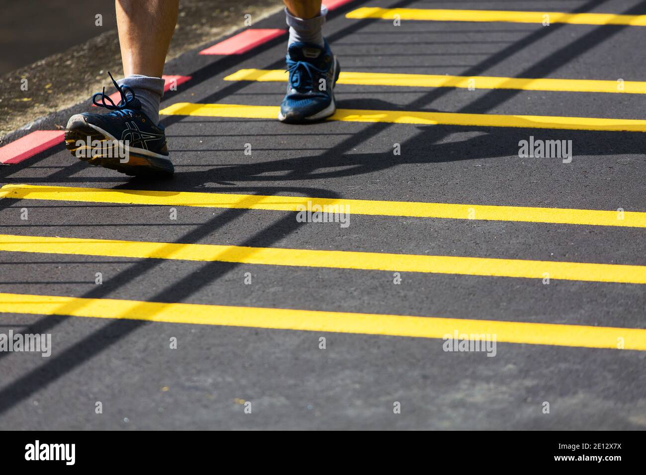 Primo piano di scarpe da running che camminano sul terreno asfaltato con strisce gialle in corrispondenza di un connettore di parcheggio. Singapore Foto Stock