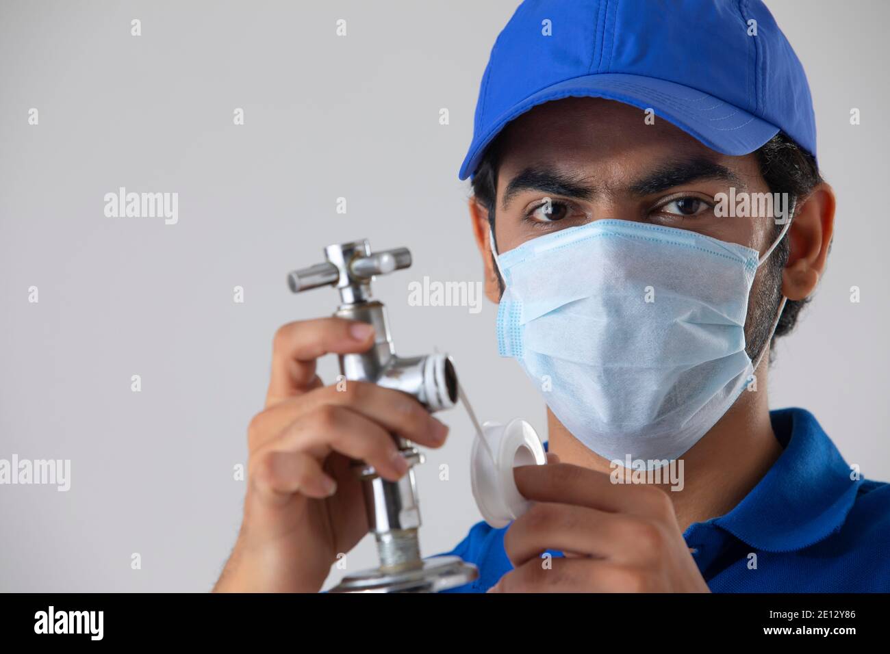 UN IDRAULICO CHE INDOSSA LA MASCHERA FACCIALE GUARDANDO LA FOTOCAMERA DURANTE LA RIPARAZIONE TOCCARE Foto Stock