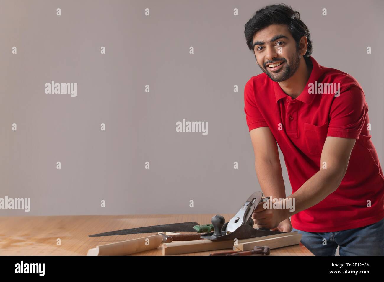 UN GIOVANE FALEGNAME SORRIDENTE ALLA MACCHINA FOTOGRAFICA MENTRE LAVORA Foto Stock