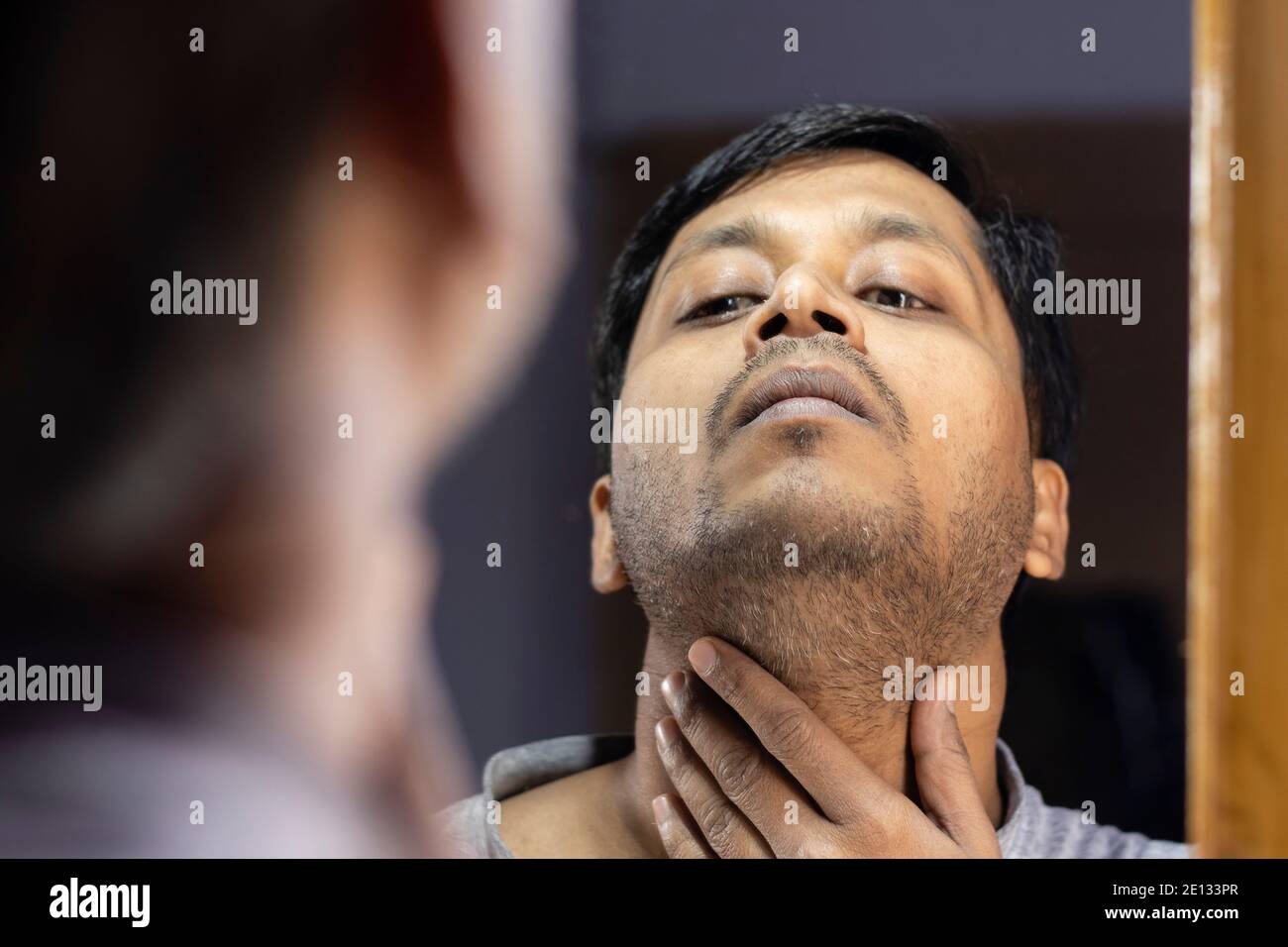 Un uomo indiano di mezza età che guarda il suo proprio unshaven barba nello specchio Foto Stock