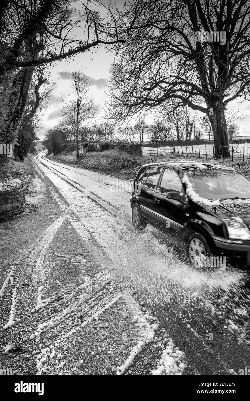 Auto che viaggia lungo una strada di campagna di scongelamento della neve. Foto Stock