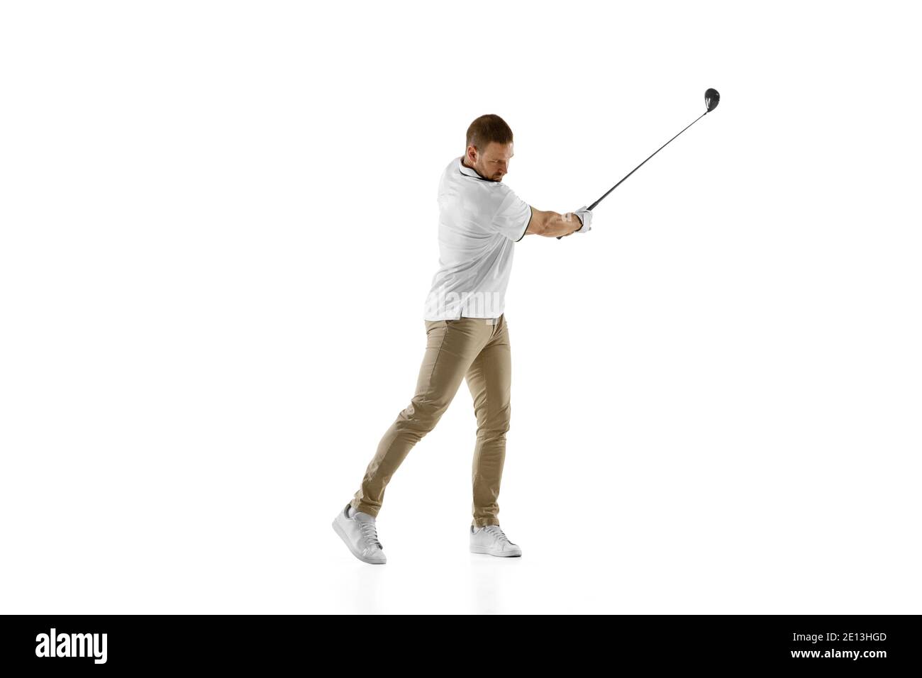 Impressionato. Giocatore di golf in una camicia bianca che prende un'oscillazione isolata su sfondo bianco dello studio con copyspace. Giocatore professionista che pratica con emozioni brillanti ed espressione facciale. Concetto di sport. Foto Stock