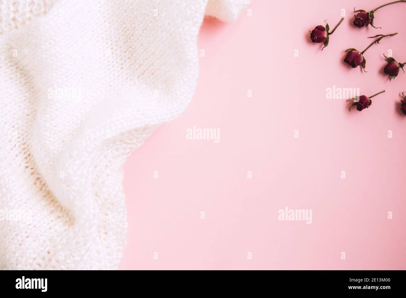 San Valentino sfondo. Gemme in miniatura di rosa rossa e tessuto bianco lavorato a maglia su sfondo rosa pastello. Concetto di giorno di San Valentino. Piatto con copia spa Foto Stock