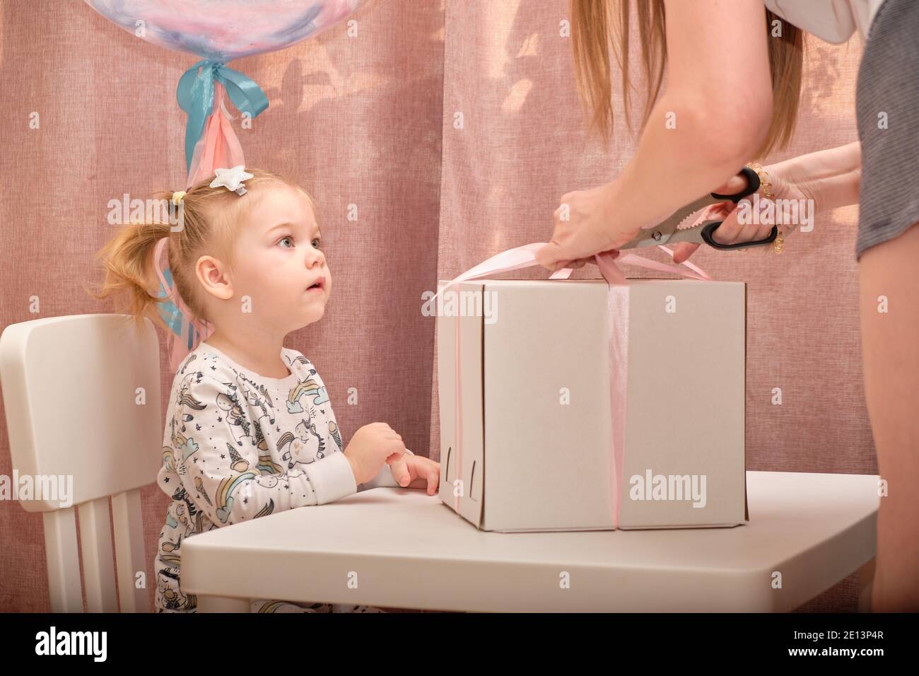 Una bambina in pigiama al suo compleanno si siede su una sedia bianca ad un tavolo per bambini, su cui c'è una nascita Foto Stock