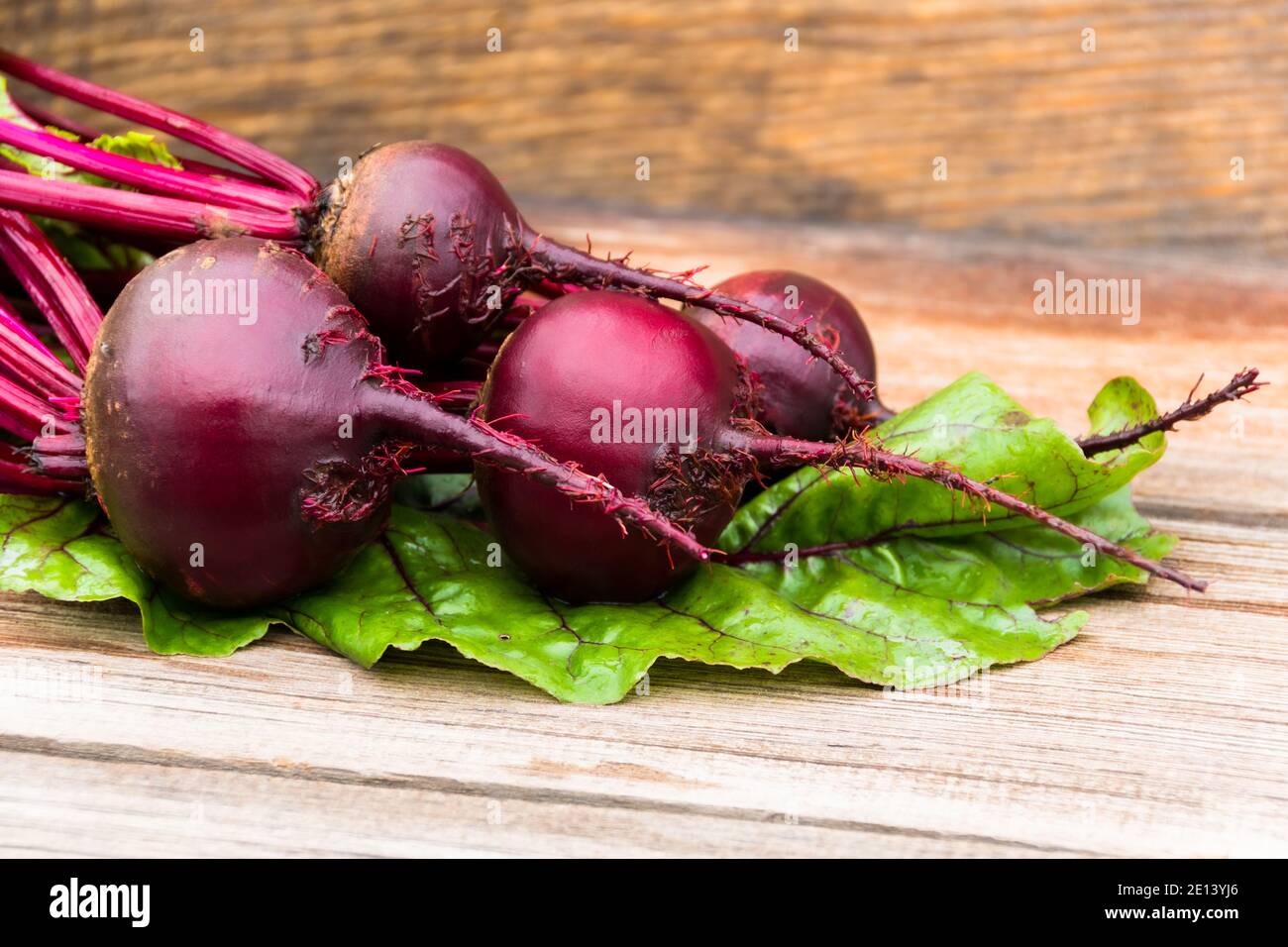 Tuberi di barbabietole con foglie verdi su tavola di legno. Preparazione di insalata fresca. Verdure fresche per la cucina vegetariana. Barbabietole sul mercato di strada. Foto Stock