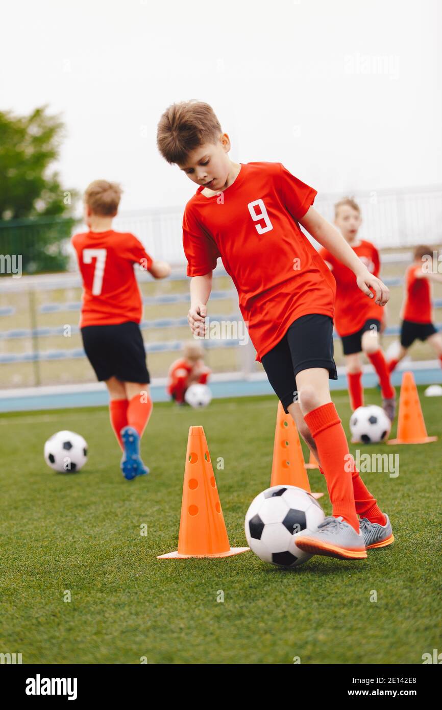 I ragazzi calciano le palle da calcio in allenamento all'aperto. Gruppo di giovani giocatori di calcio che praticano abilità di dribbling running palle tra coni di allenamento. Giovani Foto Stock