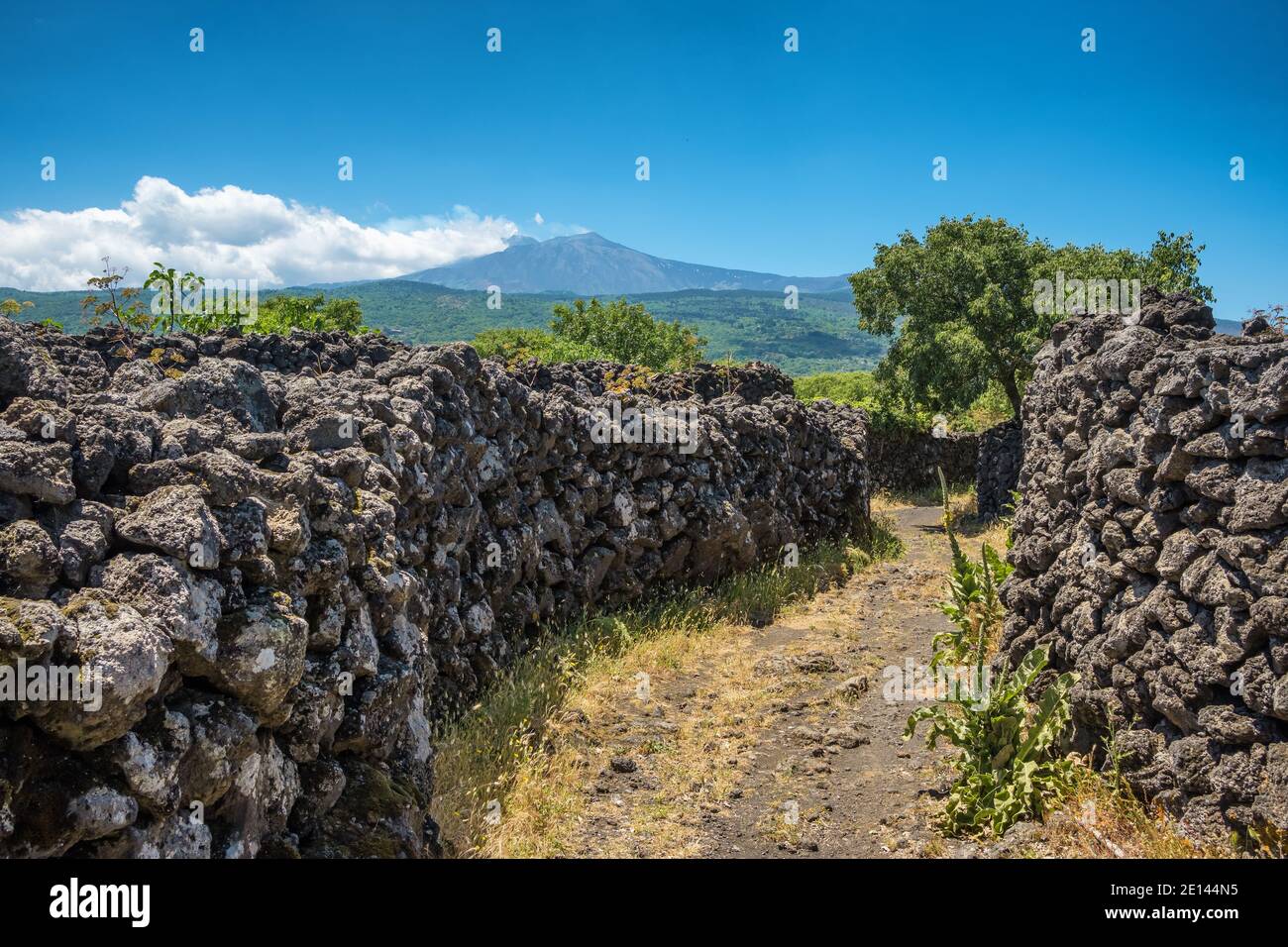 Strada rurale lungo il vecchio muro di pietra lavica con il vulcano Etna Vista in Sicilia Foto Stock