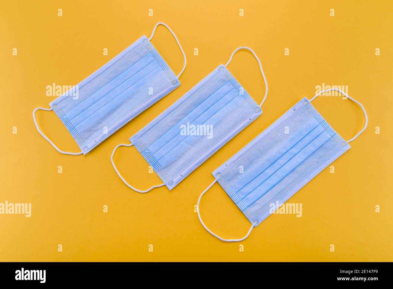 Maschere chirurgiche su sfondo giallo. Maschera medica per protezione Covid-19 per prevenire pandemie di coronavirus, vista dall'alto Foto Stock