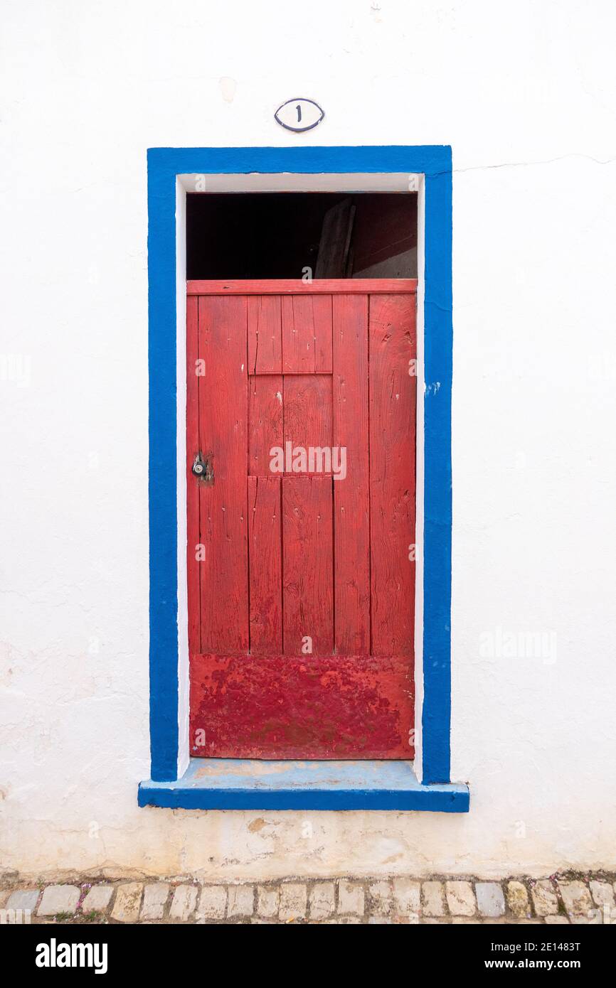 Vecchia porta rossa con telaio blu su un bianco Muro nel villaggio di Alte l'Algarve Portogallo con Casa numero uno sopra la porta Foto Stock