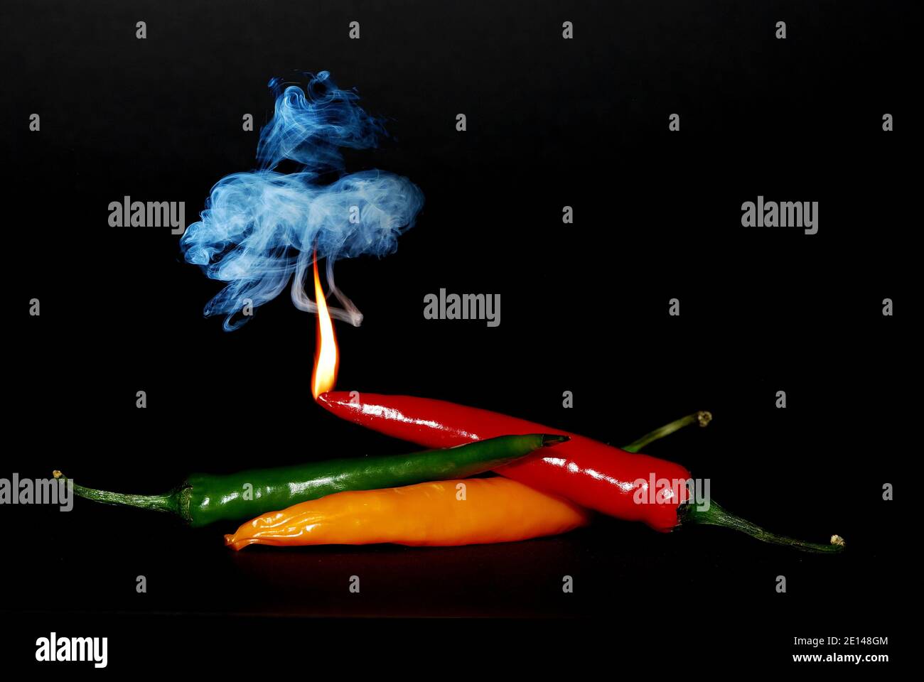 tre peperoncini di colore diverso con fiamma e fumo sfondo nero Foto Stock