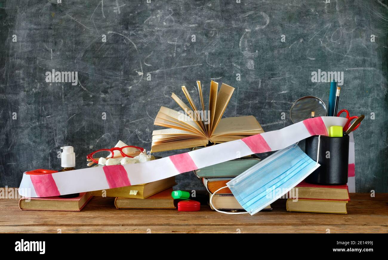 Arresto scolastico, durante la pandemia corona, scrivania con libri e forniture scolastiche, nastro barriera, maschera facciale e disinfettante Foto Stock