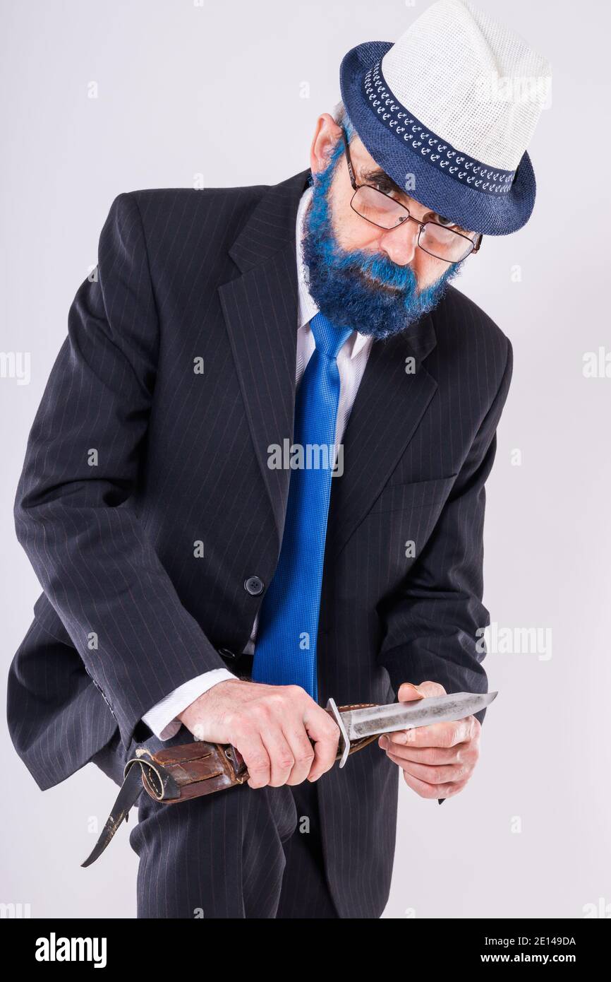 Un uomo anziano in bicchieri con barba blu regge un coltello enorme tra le mani e sembra spaventosamente sotto la fronte Foto Stock