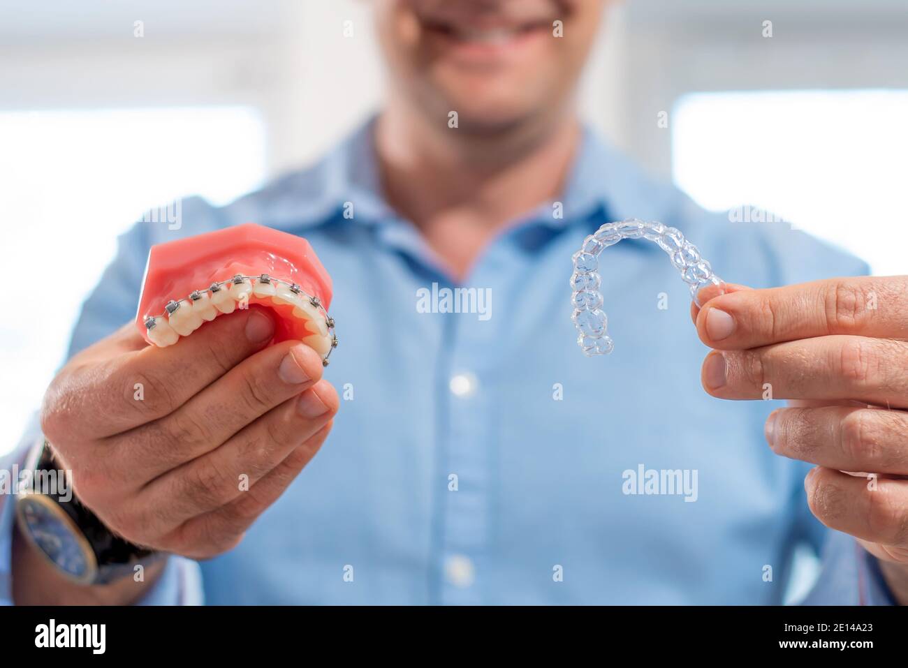 Dental care.smiling medico ortodontista che tiene aligners e bretelle in mano mostra la differenza tra loro Foto Stock