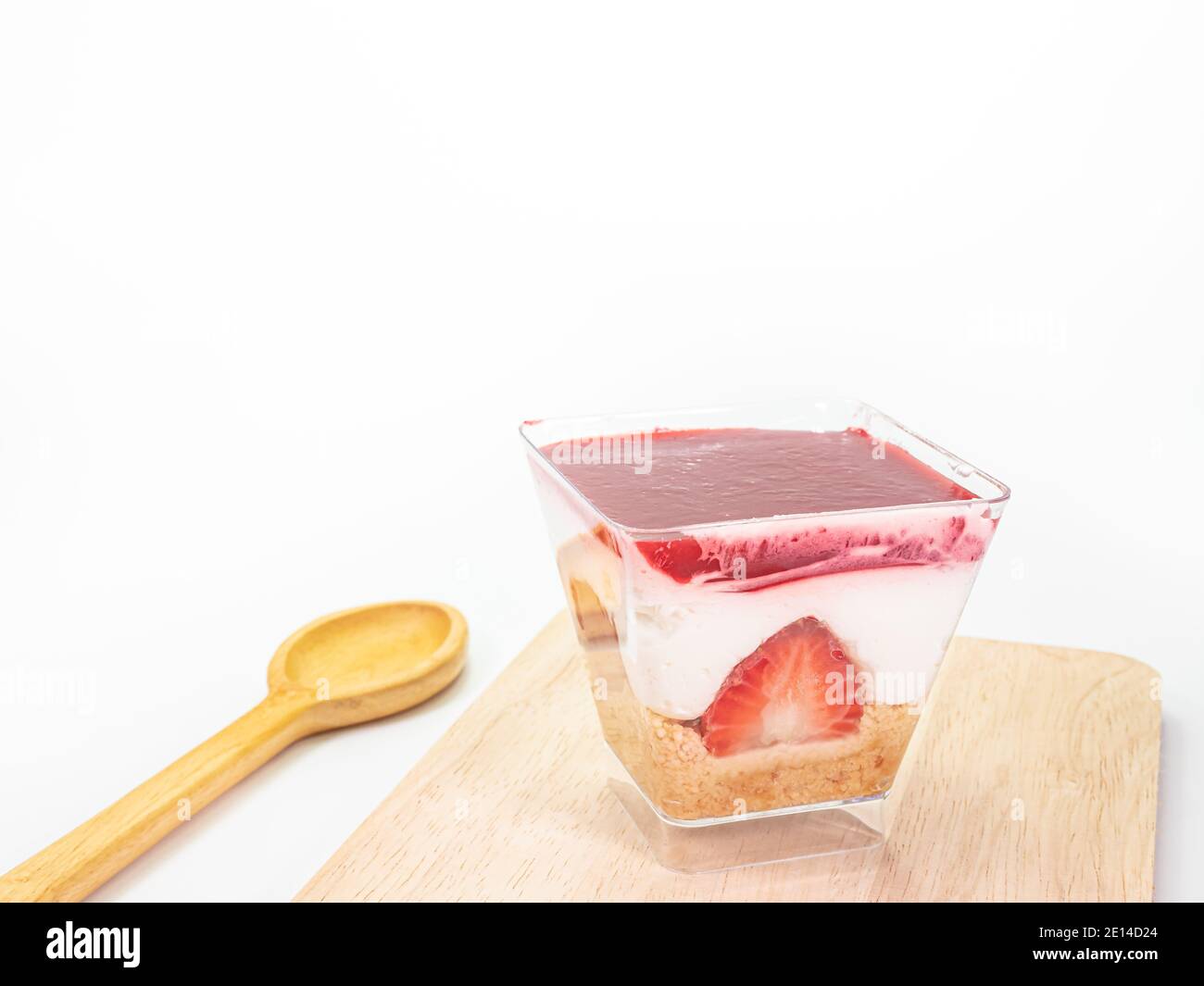 Primo piano della cheesecake alla fragola in una tazza trasparente di plastica quadrata su tavola di legno su sfondo bianco. Foto Stock