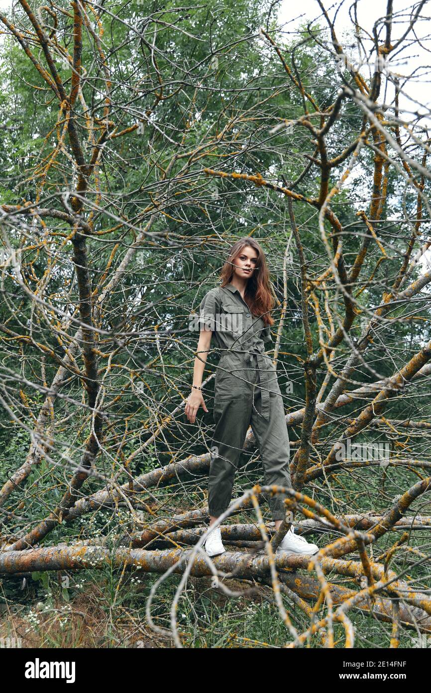 donna in sneakers e un completo jumpsuit su un rotto albero nella foresta Foto Stock