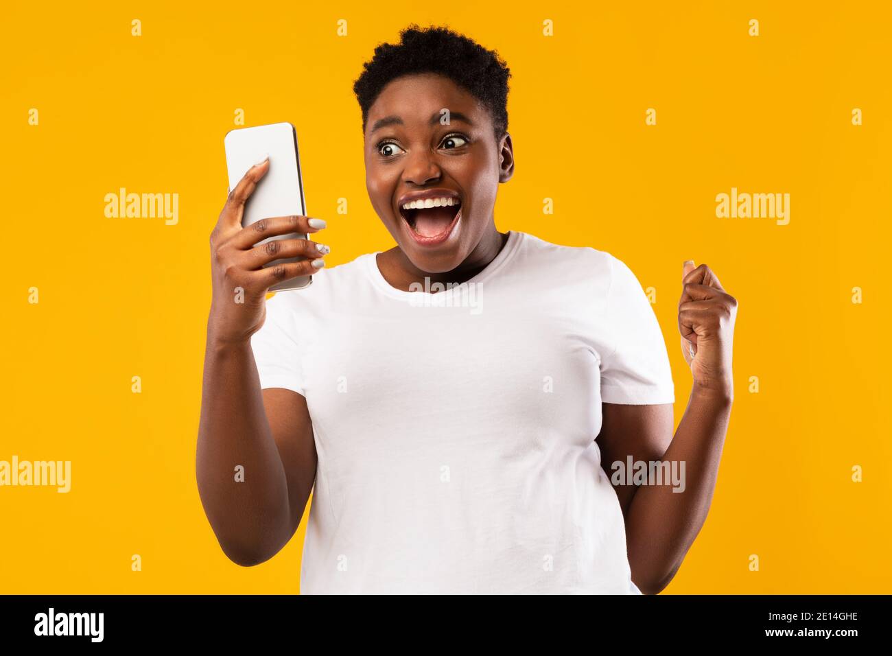 African Woman Holding smartphone scuotere Fisti in gioia, sfondo giallo Foto Stock