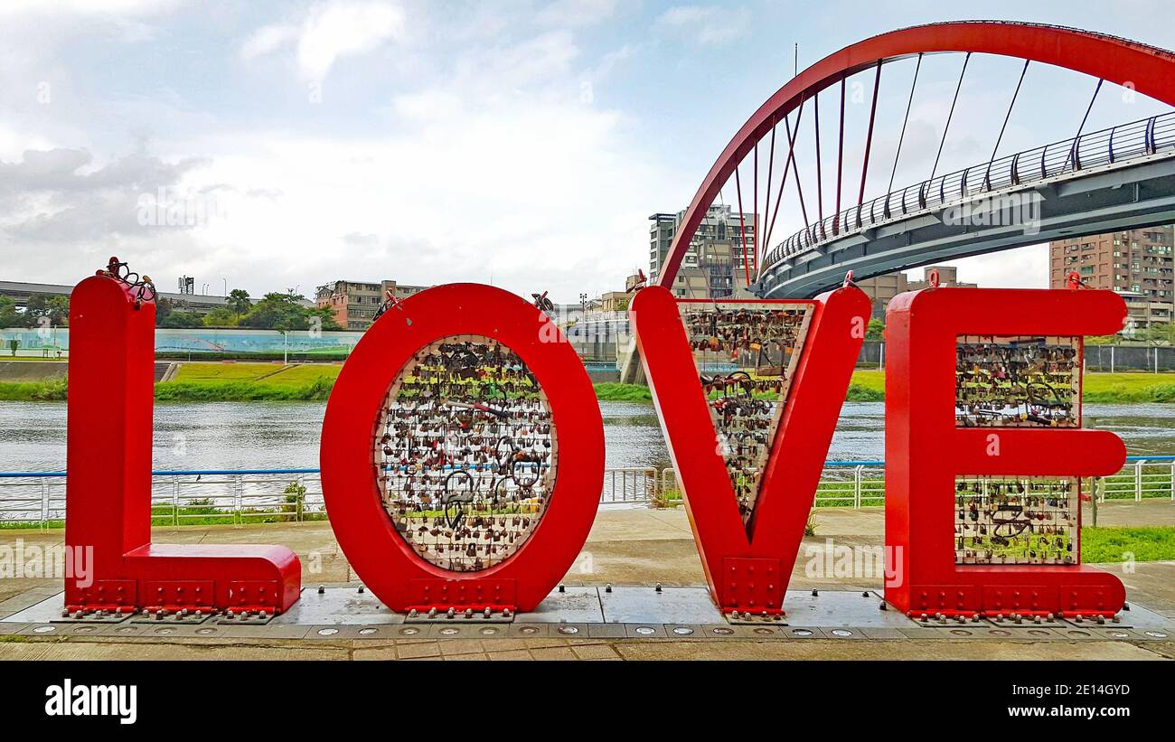 Le lettere rosse AMANO la riva del fiume a Taipei con lucchetti colorati davanti al ponte rosso Foto Stock