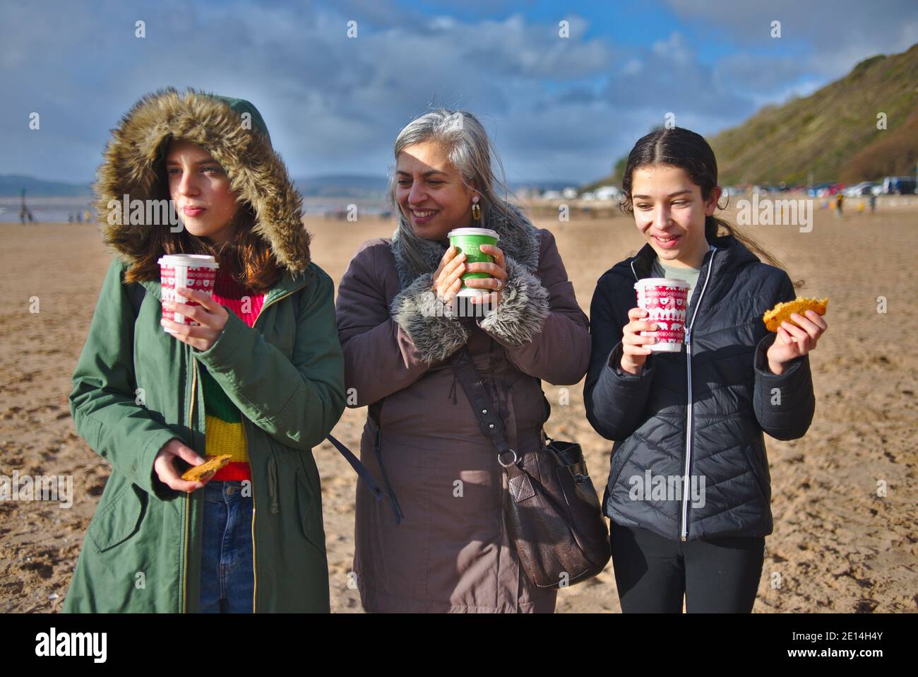 Madre e figlie che si godono una passeggiata invernale sulla spiaggia con cioccolatini caldi e biscotti. Foto Stock