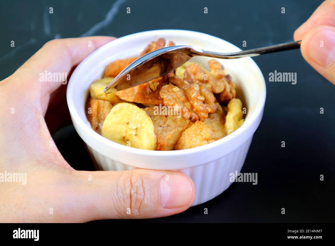Scopare a mano il pane di noce di banana pudding in una ciotola di ceramica Su tavolo nero Foto Stock