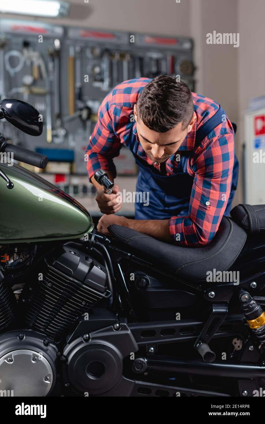 giovane meccanico che tiene la chiave a bussola durante l'esame della motocicletta in officina Foto Stock