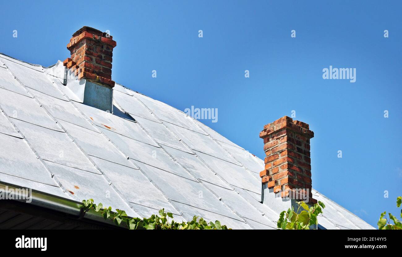 Il foglio di metallo grigio tetto con due camini tradizionale in mattoni su una casa in campagna con un cielo azzurro sfondo, spazio di copia Foto Stock