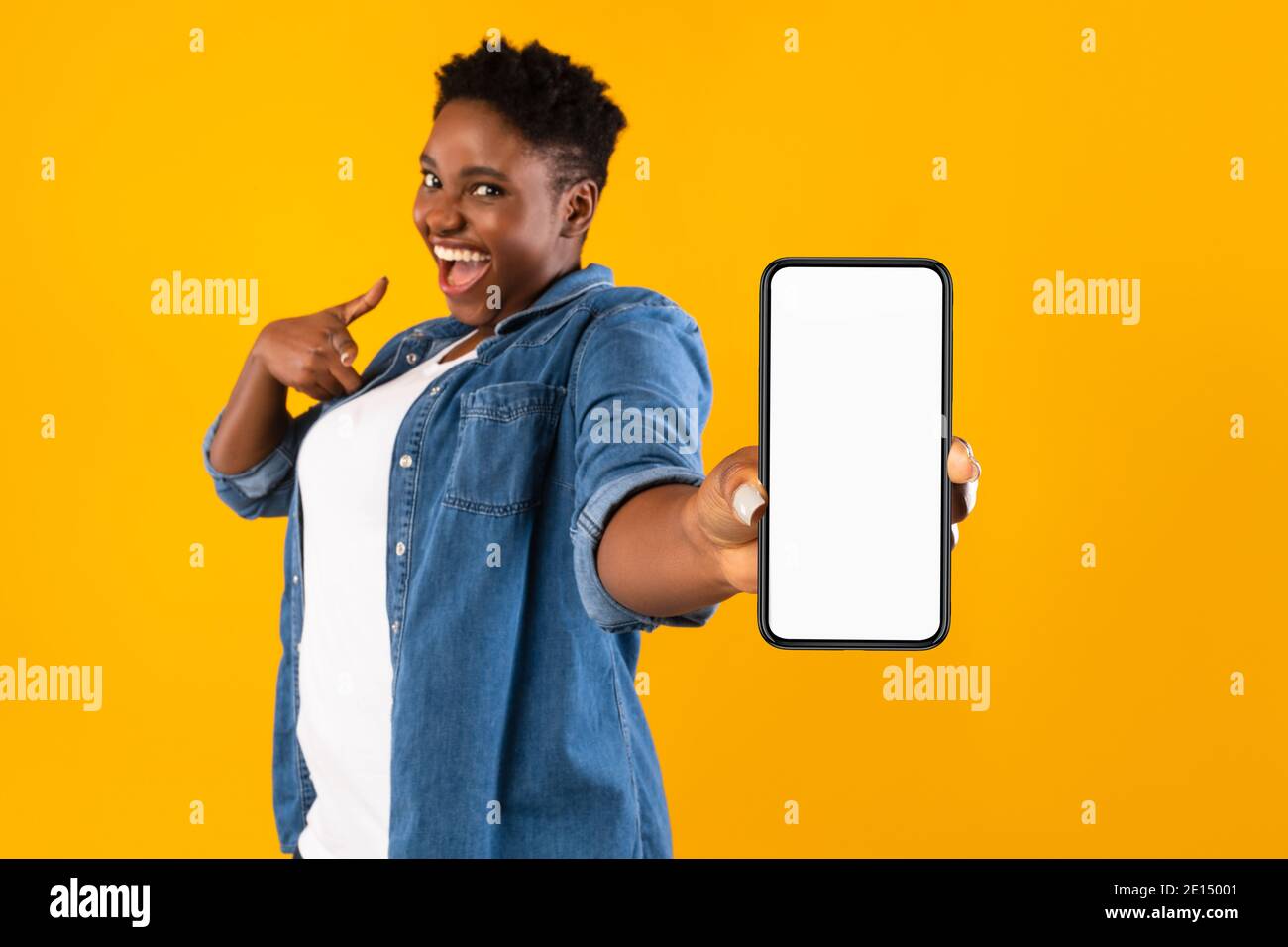 Donna Africana eccitato che mostra lo schermo del telefono che raccomanda l'applicazione, sfondo giallo Foto Stock