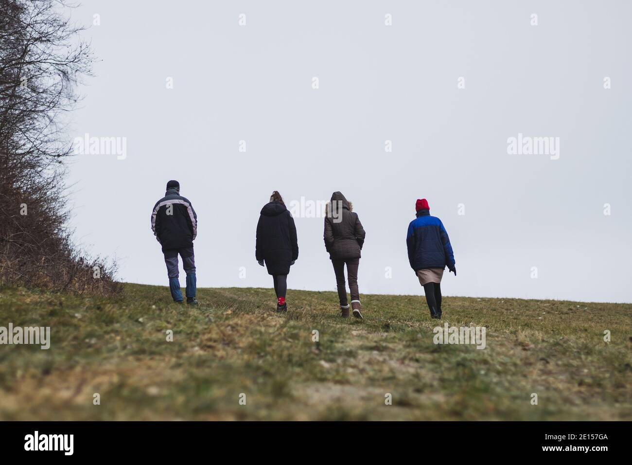 Un gruppo di persone cammina fianco a fianco attraverso la campagna in tempo freddo, vista posteriore Foto Stock