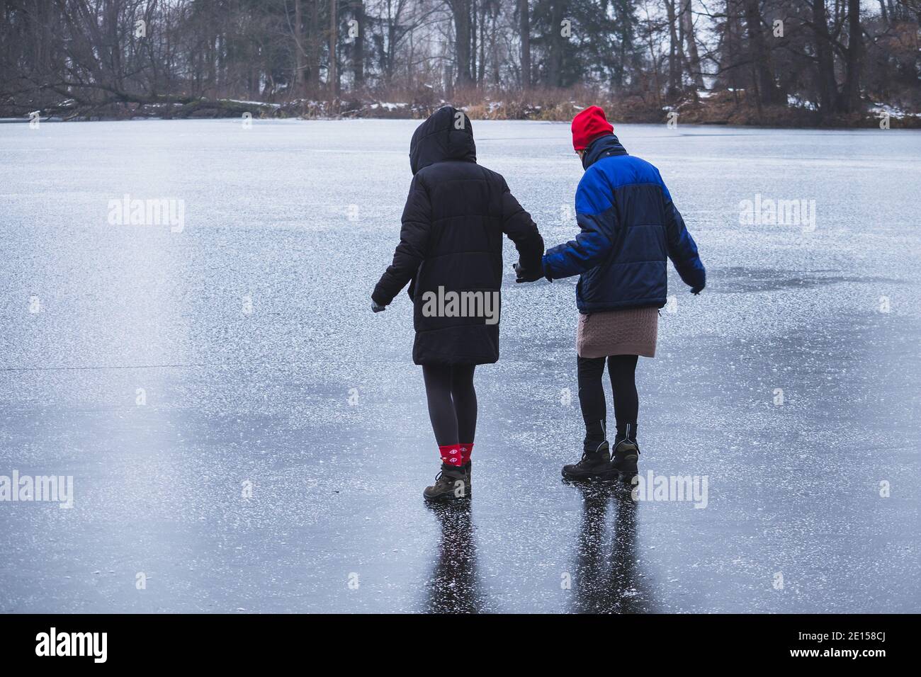 due donne che tengono le mani, camminano attentamente sul ghiaccio insieme Foto Stock