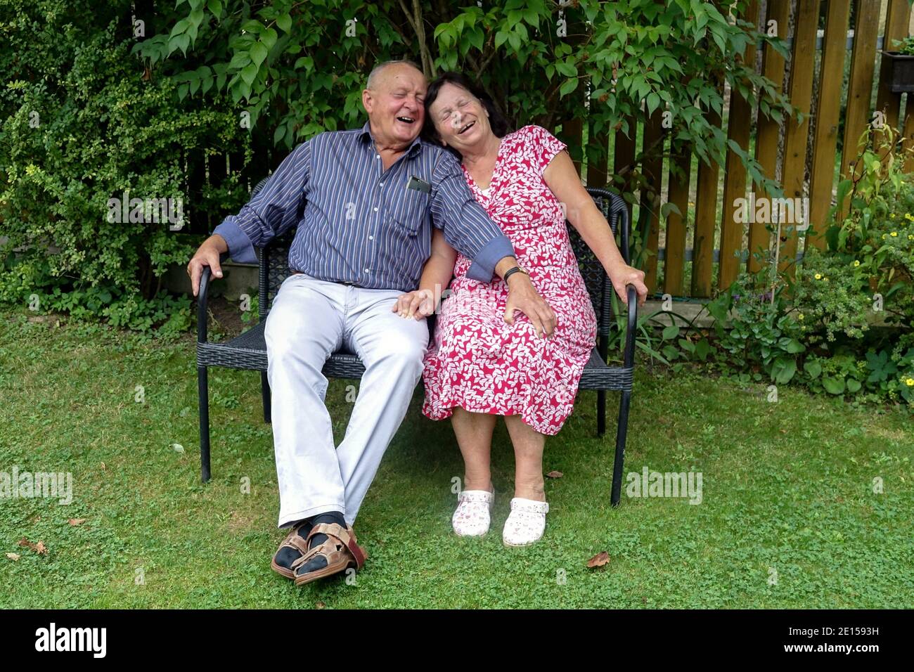 Ridendo coppia anziana seduta su una panchina in un giardino coppia anziana felice Foto Stock