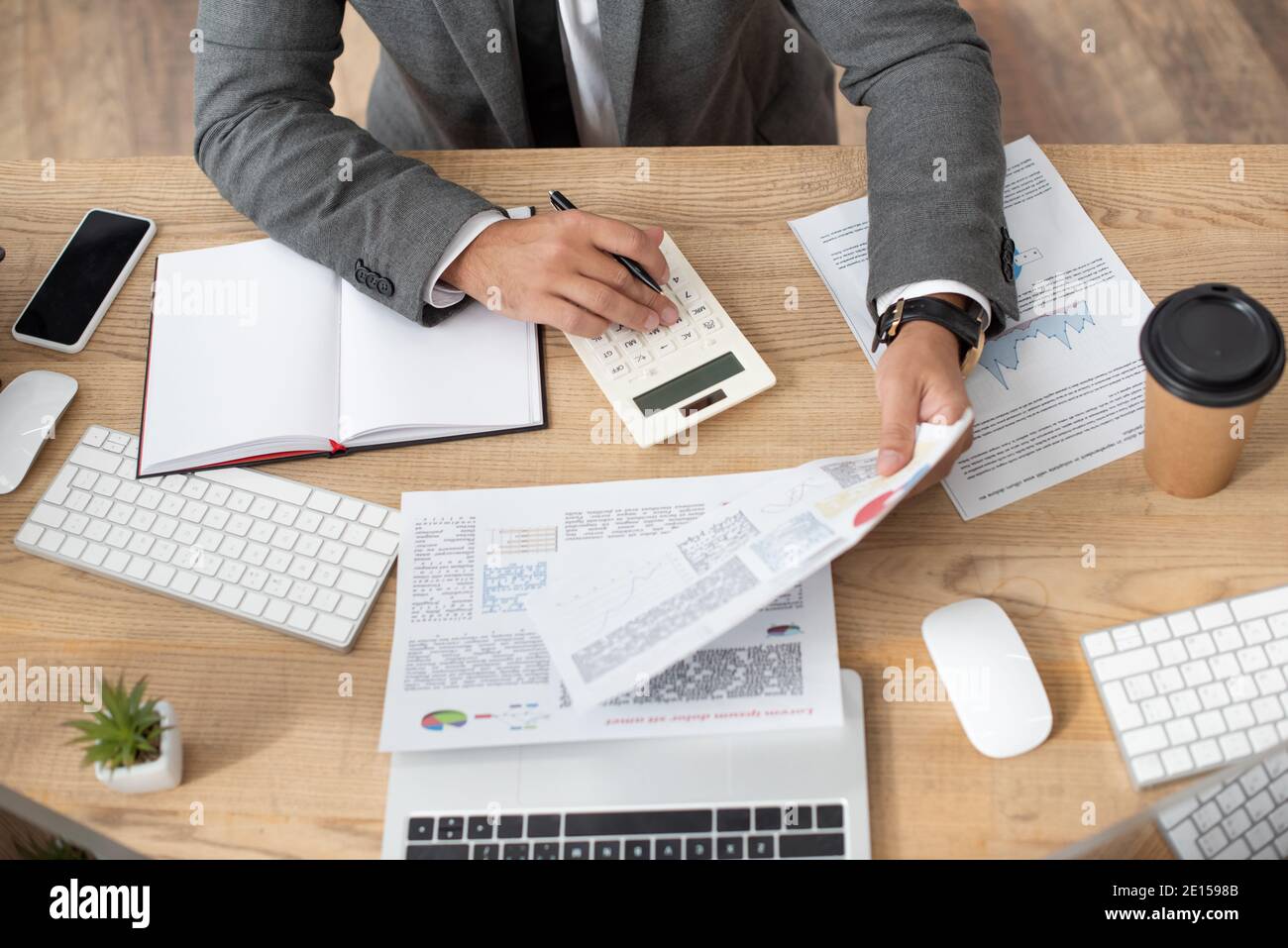vista parziale del trader che lavora con infografiche e calcolatrice vicino smartphone e tastiere Foto Stock