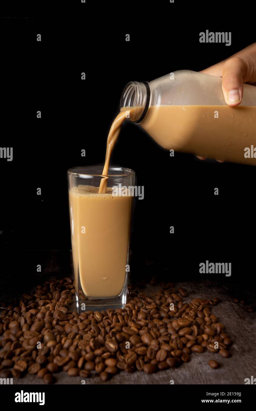 una bottiglia di latte di caffè su sfondo scuro. Il caffè tardivo viene versato nel bicchiere Foto Stock