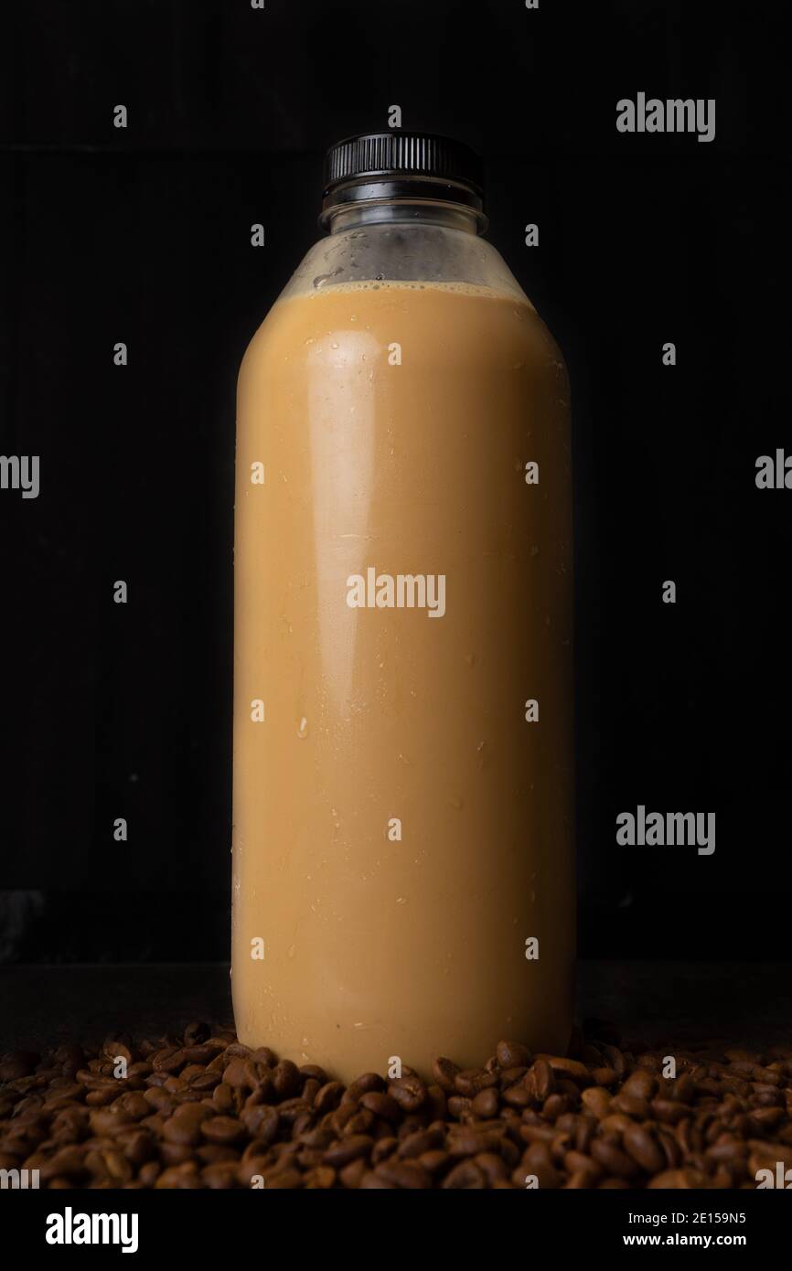 una bottiglia di latte di caffè su sfondo scuro. Il caffè tardivo viene versato nel bicchiere Foto Stock