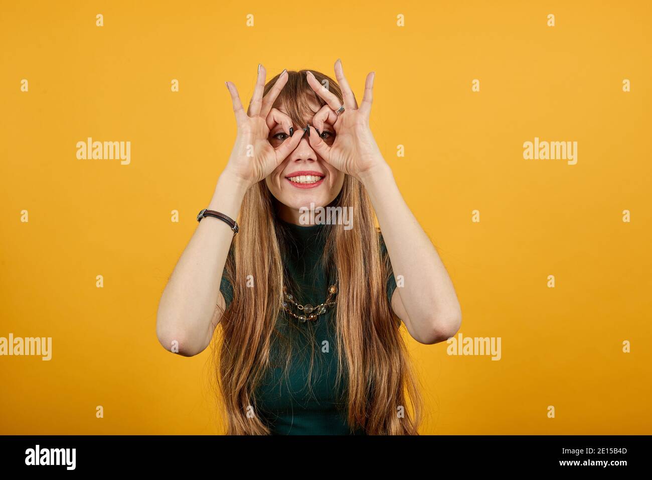 Fare occhiali di dita, guardare la macchina fotografica e sorridere, divertente, tenere le mani vicino agli occhi, imitare binocoli, tenere le sopracciglia braccio, attraverso immaginario binocolo, grimacing, maschera con la mano. Foto Stock