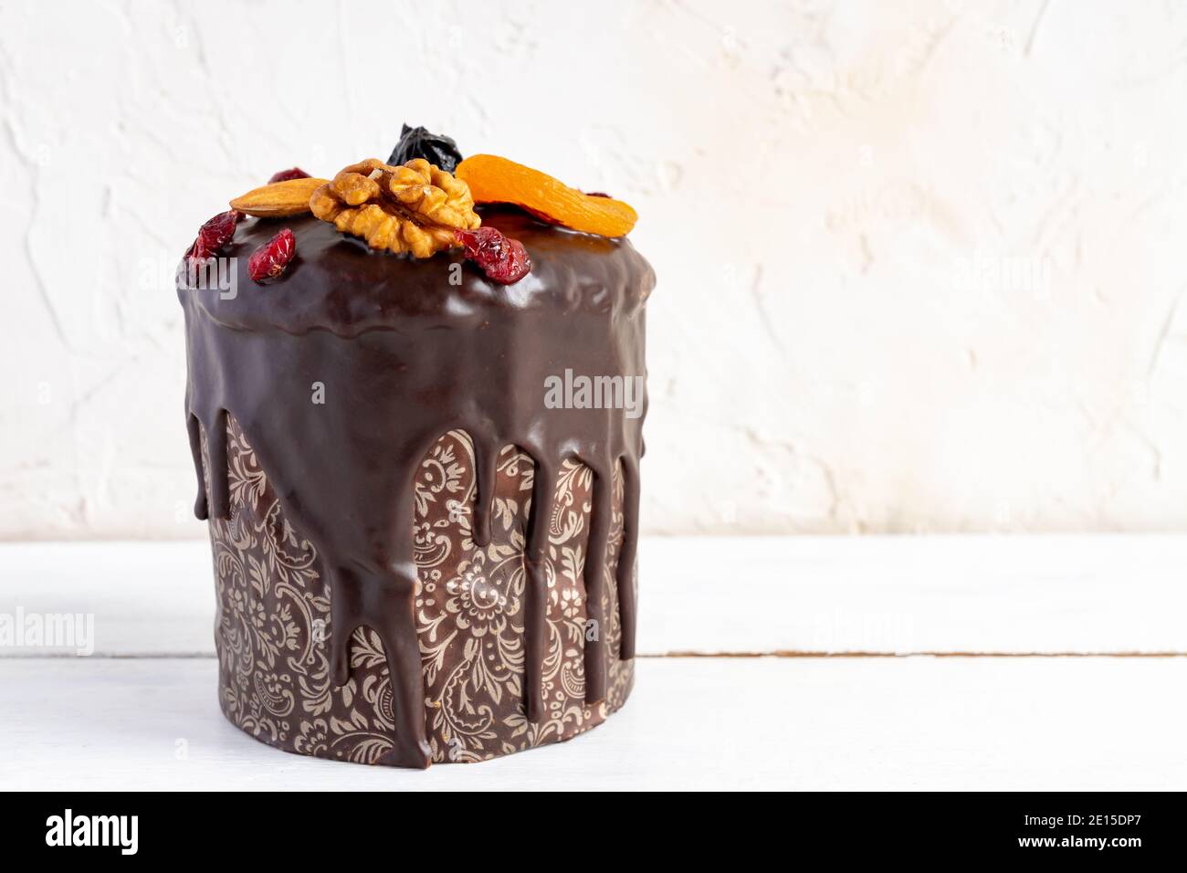 Torta di Pasqua o kulitch con glassato di cioccolato e decorato con noci, frutti secchi e frutti su tavola di legno bianco. Foto Stock