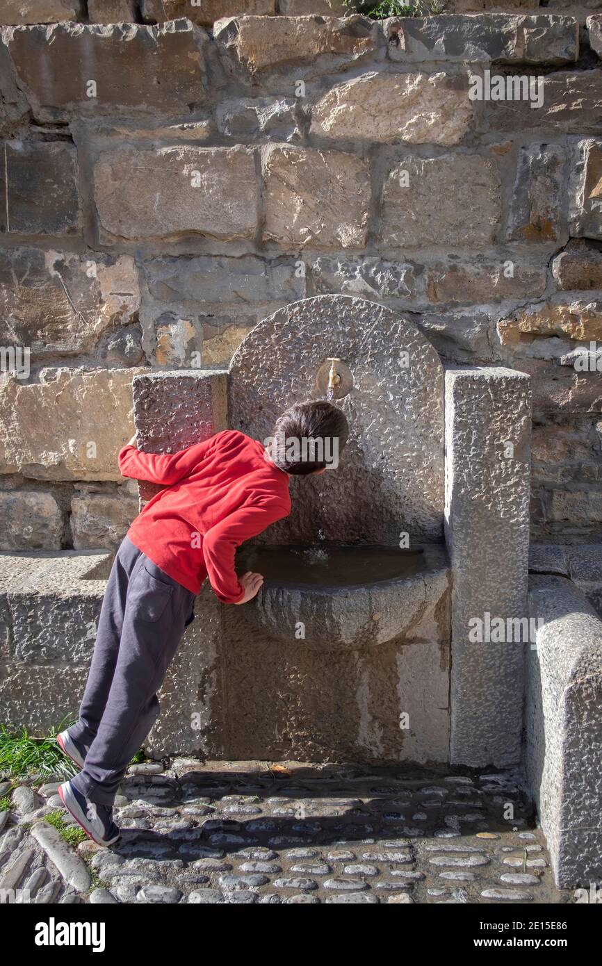 Bambino sulla schiena beve acqua sulla punta in una fontana di pietra ad Ainsa, Huesca Spagna, verticale Foto Stock