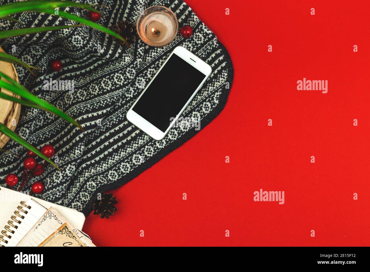 Piatto Lay accogliente composizione con maglia sfondo rosso, smartphone, candela e decorazioni, hygge concetto, copia spazio foto Foto Stock